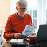 Article thumbnail: Portrait of a senior caucasian man in his 70s checking his energy bills at home. He has a worried expression while looking at the bills. Focus on the man while the interior architecture of the house is defocused.
