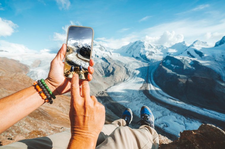 Tourist photographing the Gorner Glacier (Gornergletscher) with smartphone from top of rocks, Zermatt, Valais, Switzerland